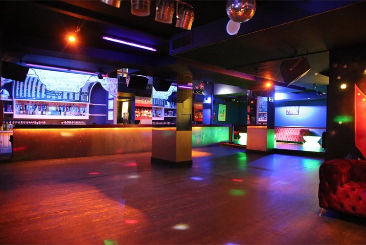 Sala Salmon en Barcelona, discoteca privada con barra retroiluminada, bola de espejos, sofá chesterfield rojo y pista de baile de madera