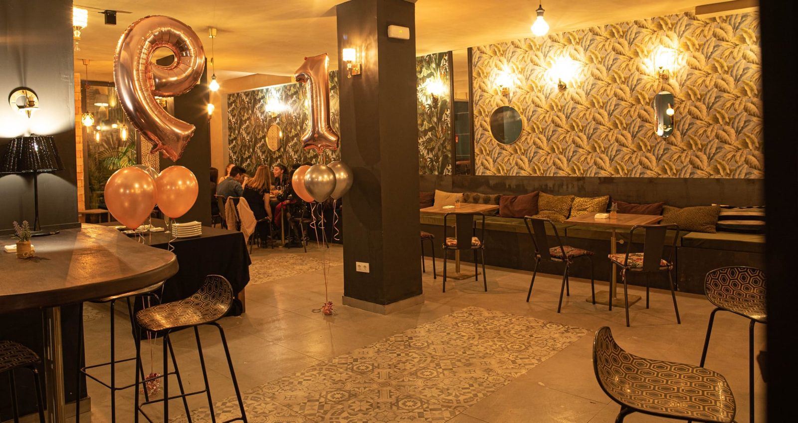 Sala Aqua Hostel en Barcelona con papel pintado botánico, apliques dorados, mesa montada con copas de cava y globos para una celebración
