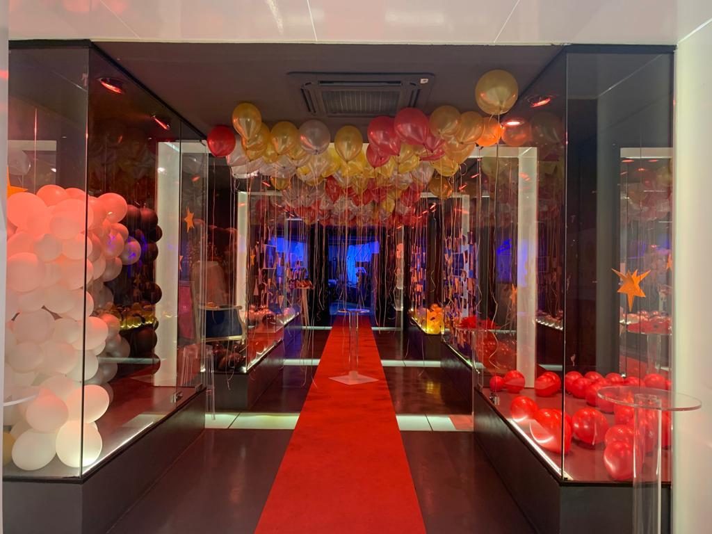 Sala Silver en Barcelona con alfombra roja, arcos de globos rojos y dorados y vitrinas de cristal iluminadas para una fiesta privada